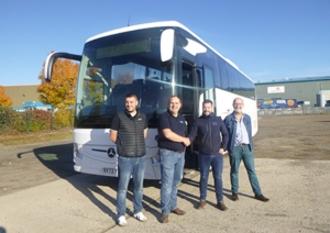 A white Mercedes-Benz coach parked up with 4 people standing in front of it