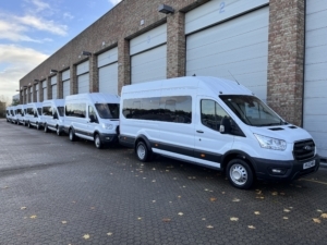 A row of white Ford Transit minibuses in front of a building