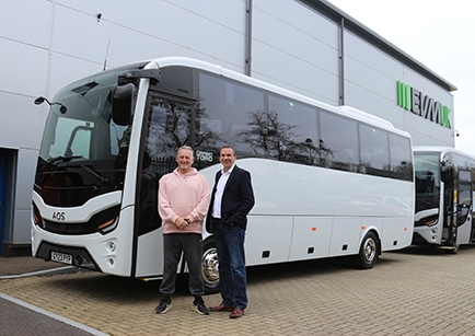 Two people standing in front of a white coach parked in front of a building