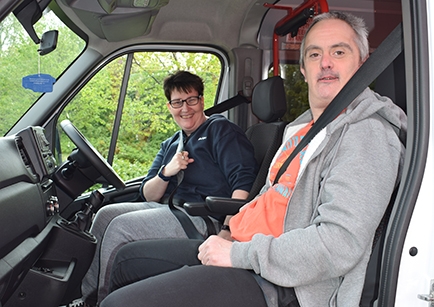 Two adults sitting in a parked white Renault minibus